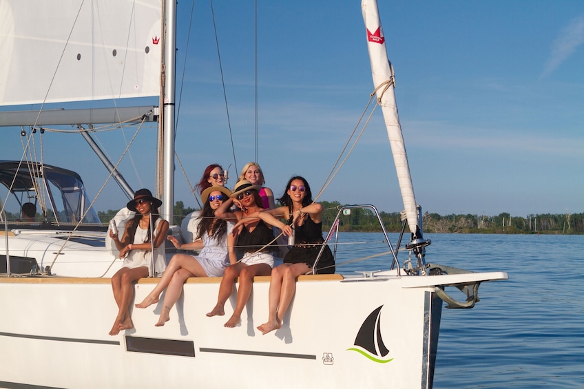 A group of people on a sailboat with a calm body of water and trees in the background. 5