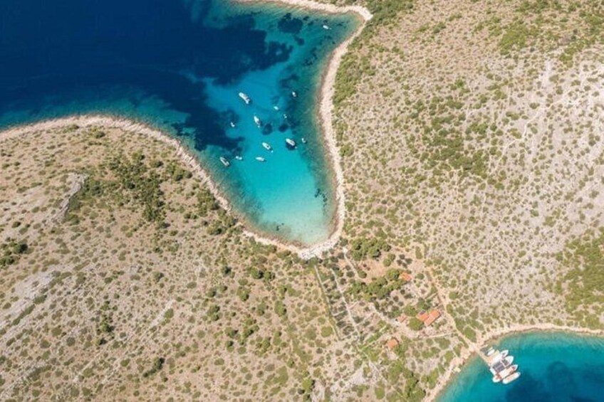 Luchtbeeld van een kustgebied met helderblauw water, een zandstrand en verspreide begroeiing. 1