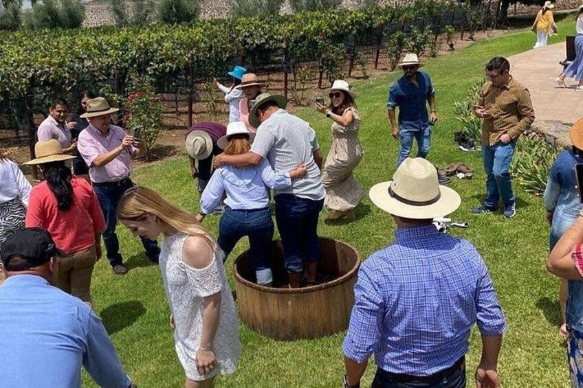 A group of people gathered outdoors, some standing and others bending over a wooden tub. 1