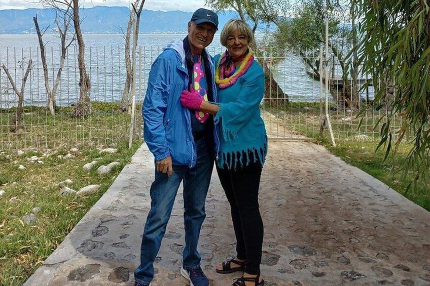 Two people standing on a concrete path by a body of water with mountains in the background. 2