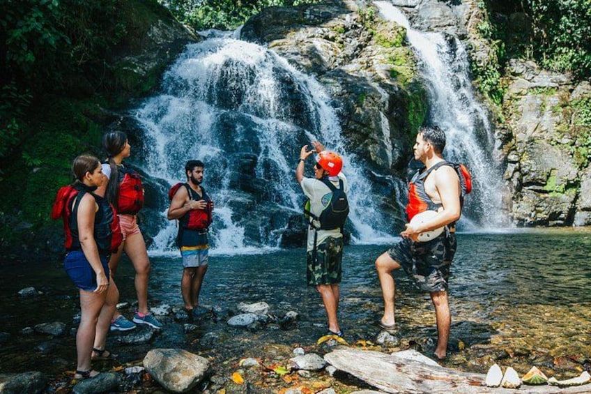 A group of people standing by a waterfall in a forested area. 1