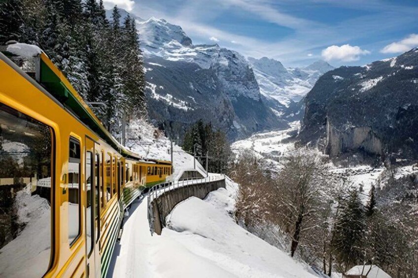 A yellow train on a snowy mountain track with snow-covered trees and mountains in the background. 5