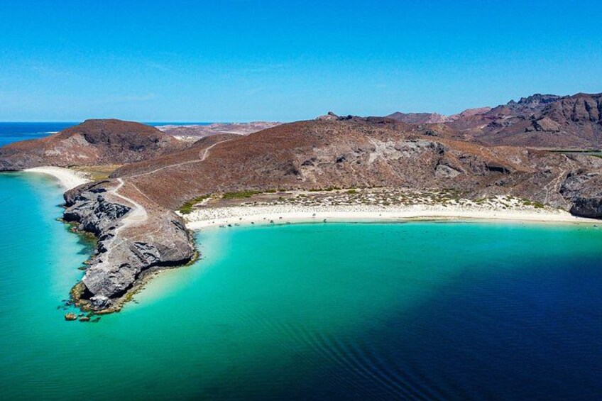 A coastal landscape with a beach, rocky terrain, and clear turquoise waters. 1