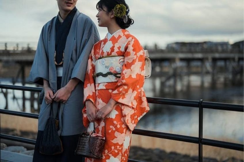 Two people in traditional Japanese attire standing by a waterfront with a bridge in the background. 3