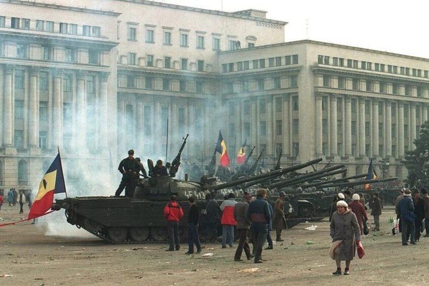 Un tanque militar con varias banderas, una multitud de personas y un edificio grande al fondo. 2