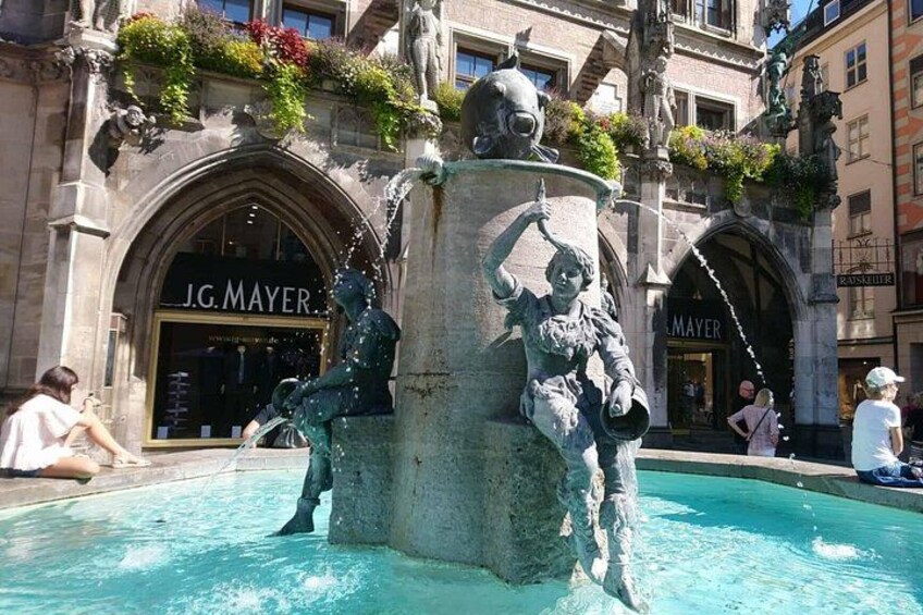 Ein Brunnen mit Statuen, ein Geschäft von J.G. Mayer und ein Gebäude mit einer Schrifttafel. 4