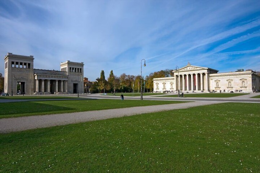 Une vaste étendue d’herbe, un espace ouvert, avec deux bâtiments de style classique, dont l’un est orné de colonnes et l’autre d’un fronton. 2
