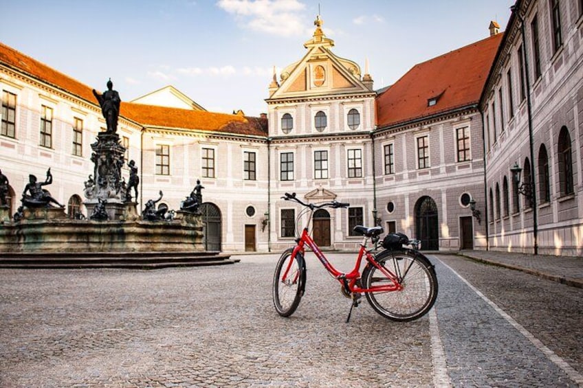 Un vélo rouge est garé devant un bâtiment historique orné d’une fontaine et de statues. 3