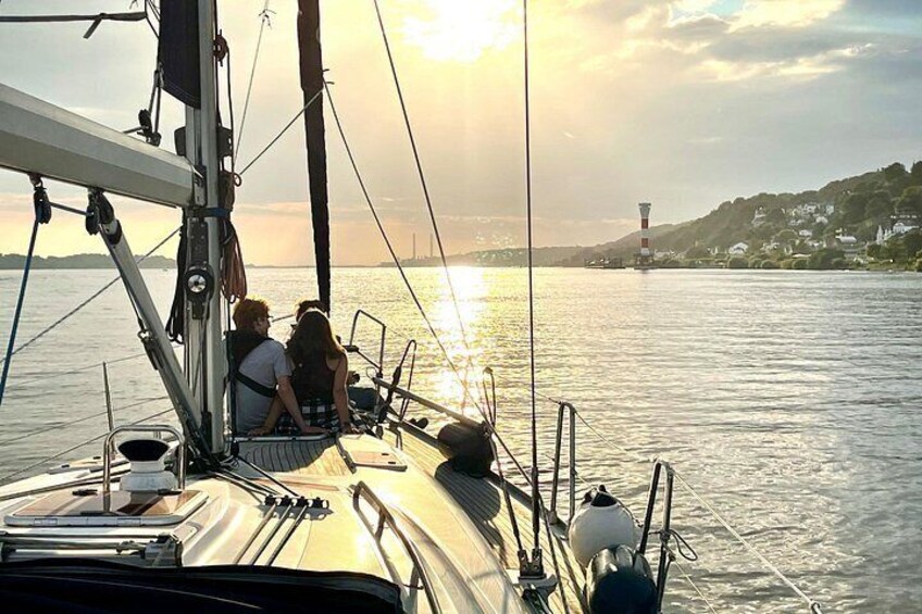Un velero con dos personas en cubierta, un faro al fondo y agua tranquila. 3