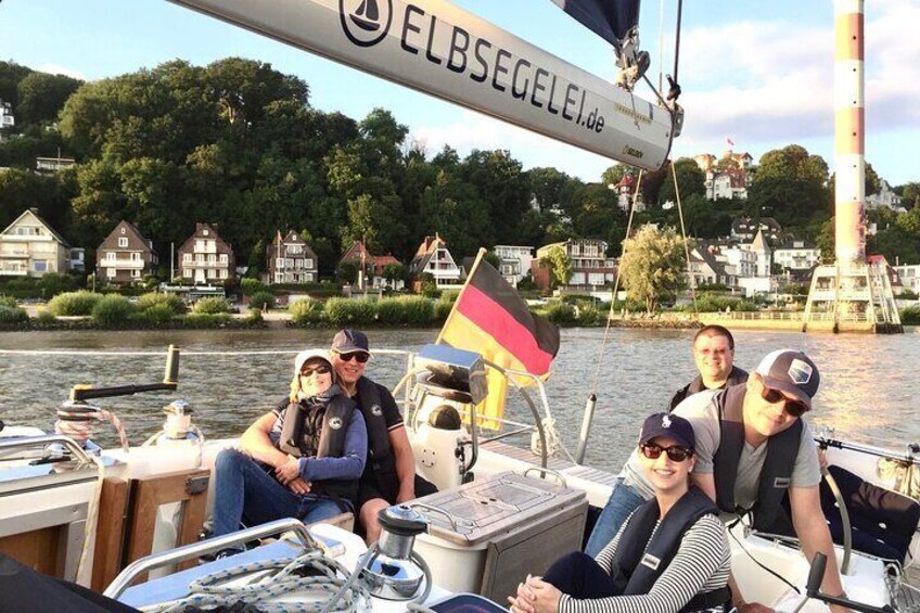 A group of people on a boat with a German flag, a waterway, and houses in the background. 5