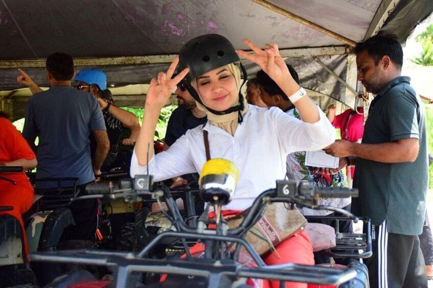 A person in a white shirt and helmet, making a peace sign, standing next to a vehicle with a microphone. 1