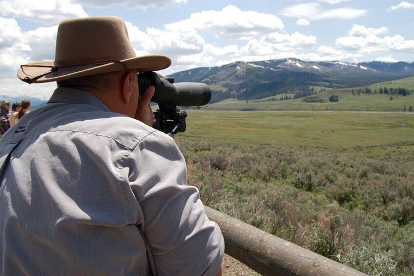 Un homme portant un chapeau, utilisant un grand appareil photo, et contemplant un paysage montagneux. 4