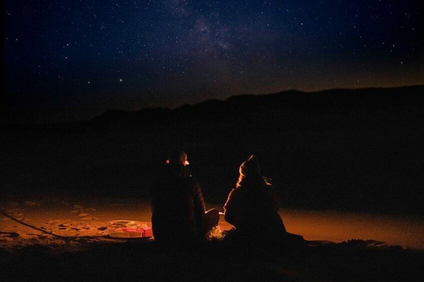 Two people sitting by a campfire at night with a starry sky above. 2