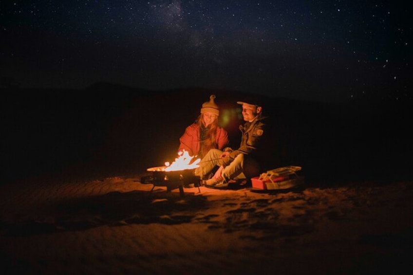 Two people sitting by a campfire at night with a starry sky. 3