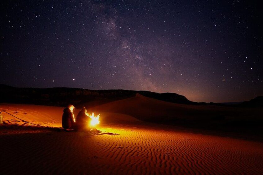 A desert landscape at night with a campfire and stars. 3
