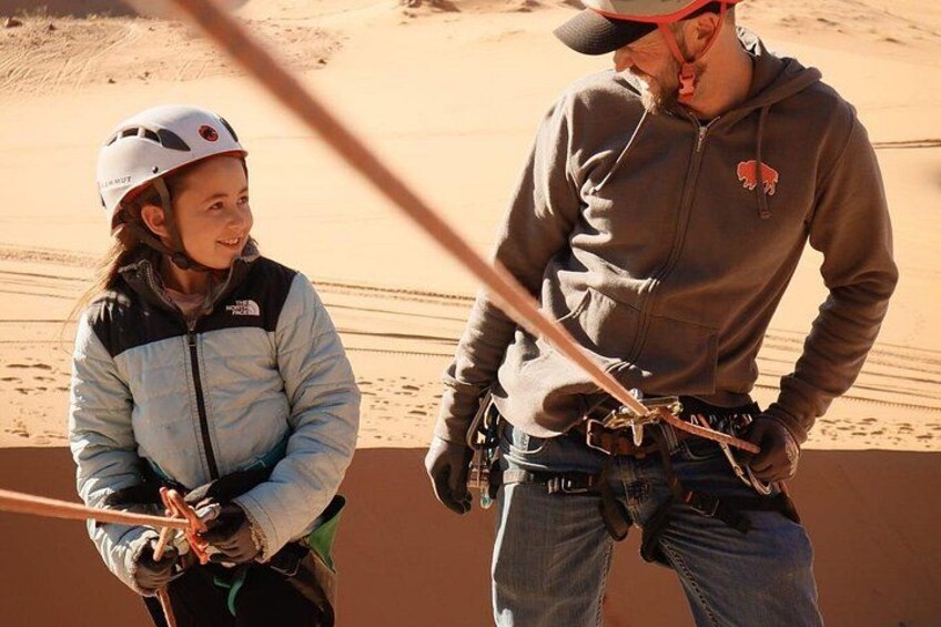 Zwei Personen in einer Wüstenlandschaft, eine mit Helm, die andere mit Kapuzenpulli, mit Seilen und Gurten. 3