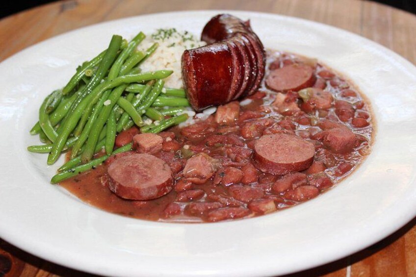 Un plato de frijoles con rebanadas de salchicha, judías verdes y una salchicha entera sobre un plato blanco. 4