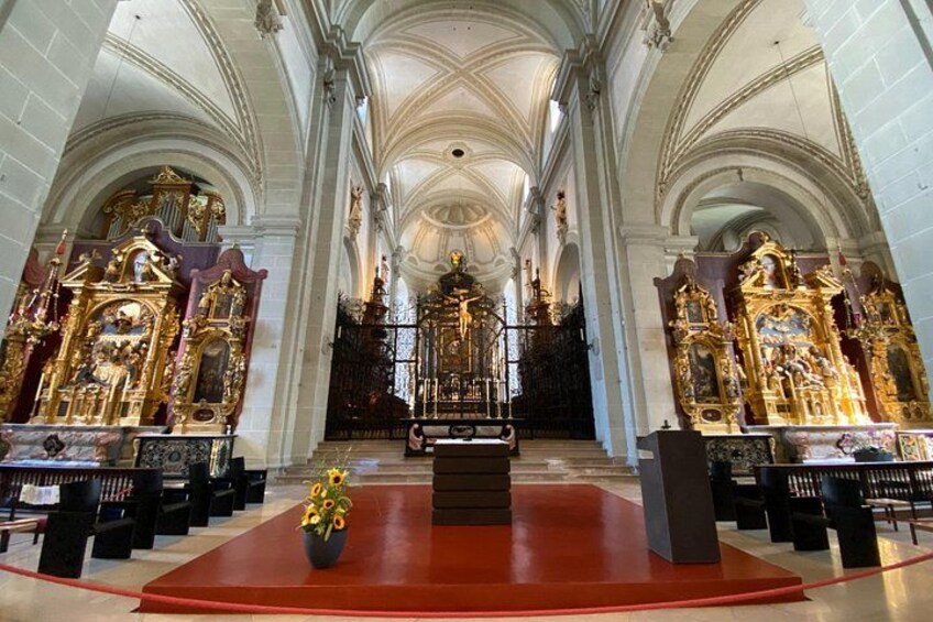 En utsmyckad kyrkinteriör med höga, välvda tak, ett centralt altare och detaljerade religiösa statyer. 2