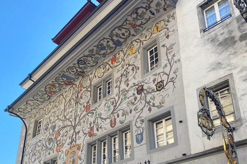 En byggnad med detaljerade väggdekorationer i form av blomstermotiv och heraldiska symboler, många fönster och ett rött tak. 3