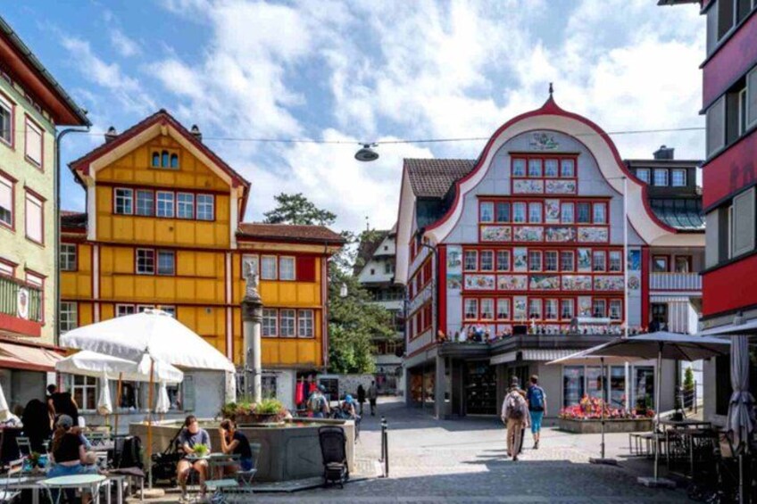 A pedestrian street with colorful buildings, outdoor seating, and a person walking. 2