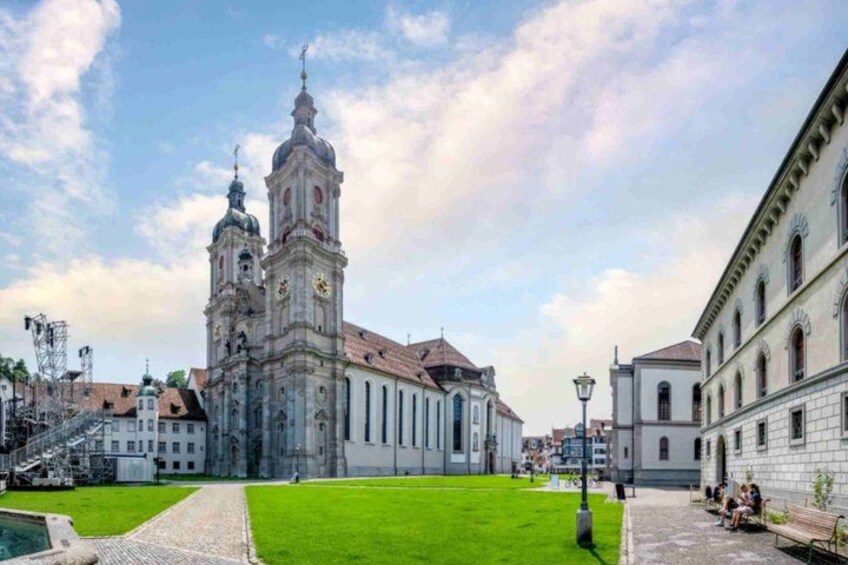 A historic church with two towers, a paved square, and surrounding buildings. 3
