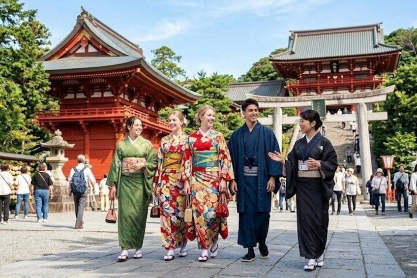 Ein traditioneller japanischer Tempel mit roten und grünen Bauwerken, Personen in traditioneller Kleidung und einem wolkenlosen Himmel. 1