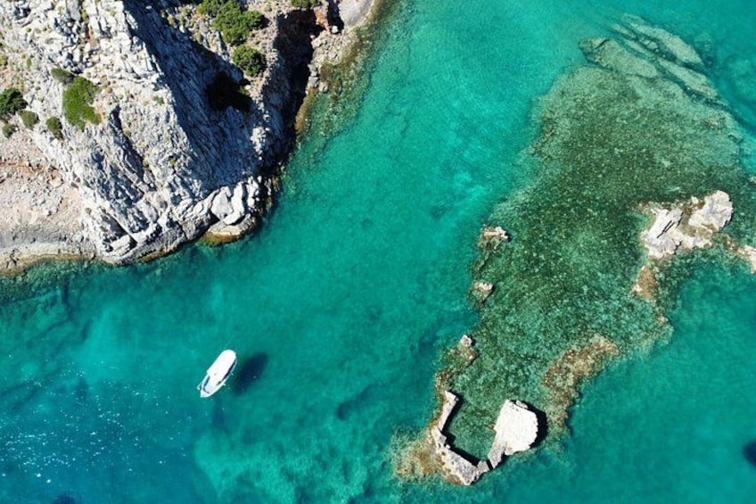 A coastal landscape with clear turquoise waters, rocky outcrops, and a small boat. 3