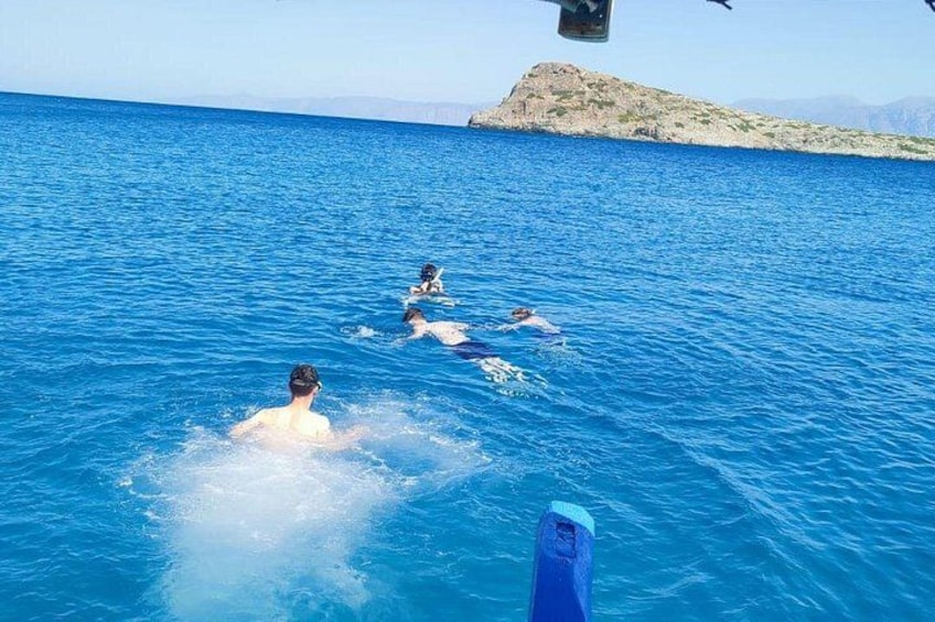 People swimming in a blue sea with a rocky island in the background. 4