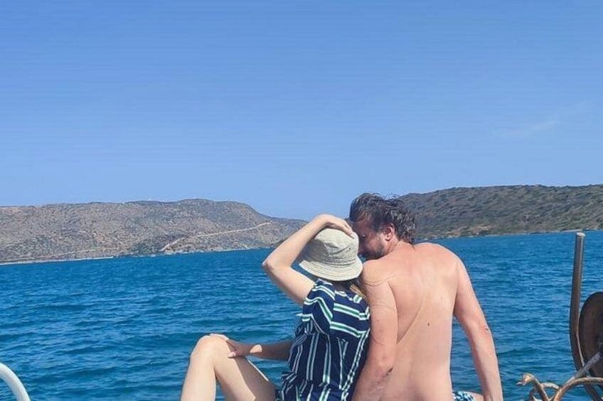 A couple on a boat with a clear blue sea and distant hills. 2