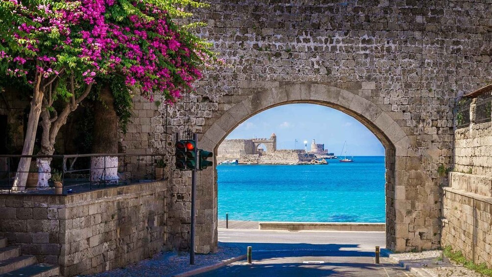 A stone archway leading to a coastal view with a historic building in the distance. 5