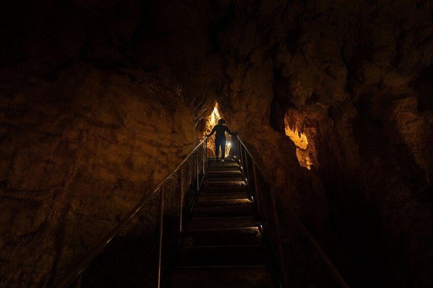A person ascending a metal staircase in a dimly lit cave with rough walls. 2