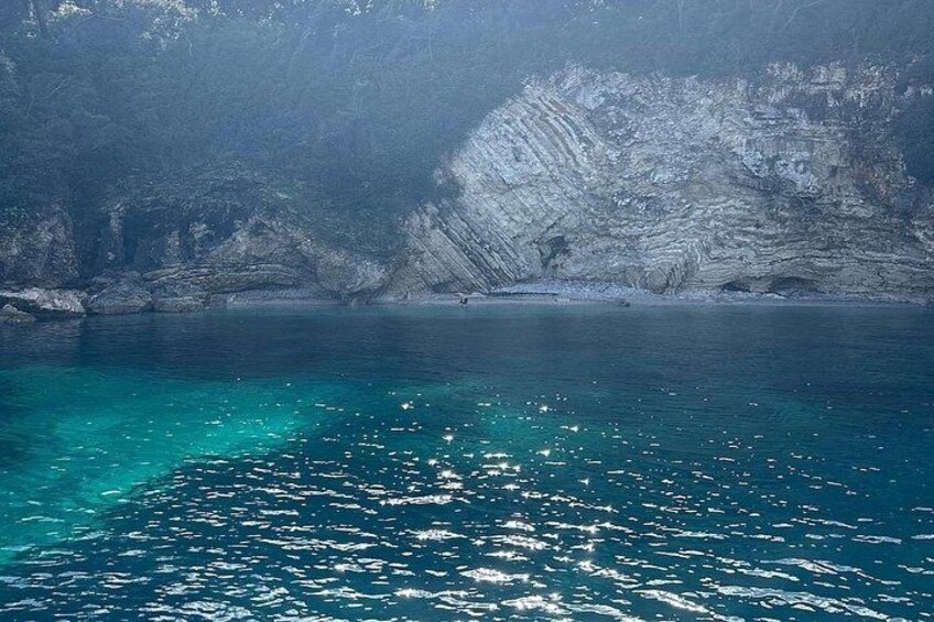 Et kystlandskab med krystalklart turkis vand, klippefremspring og en smal strand. 2