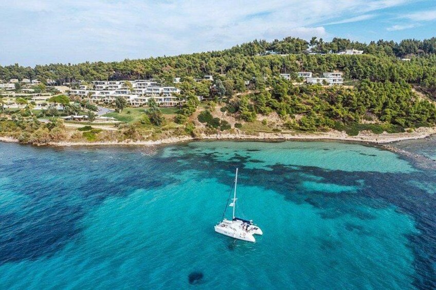 A sailboat on turquoise waters, a coastal area with buildings, and a forested hill. 2