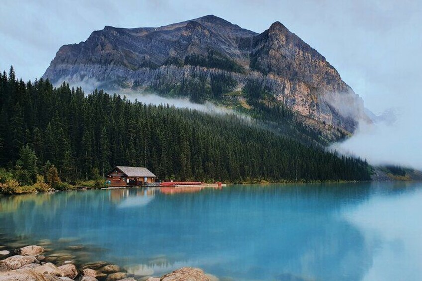 A cabin by a clear lake with mountains in the background. 1