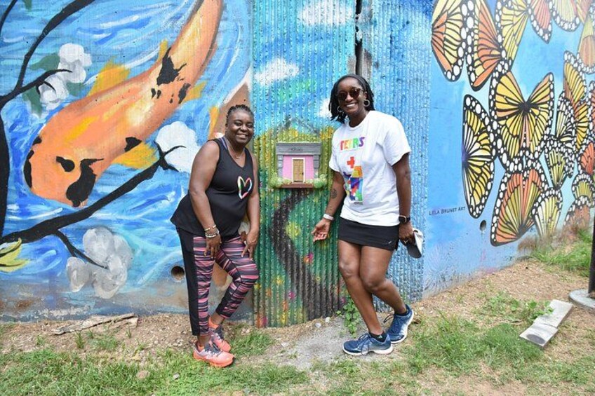 Two people standing in front of a colorful mural with butterflies and flowers. 3