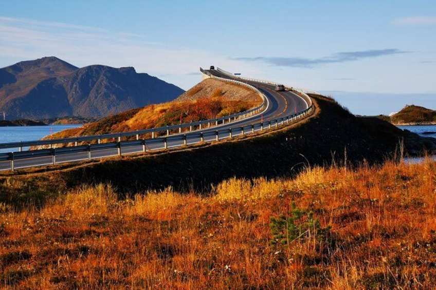 A winding road curving along a coastal landscape with mountains in the background. 2