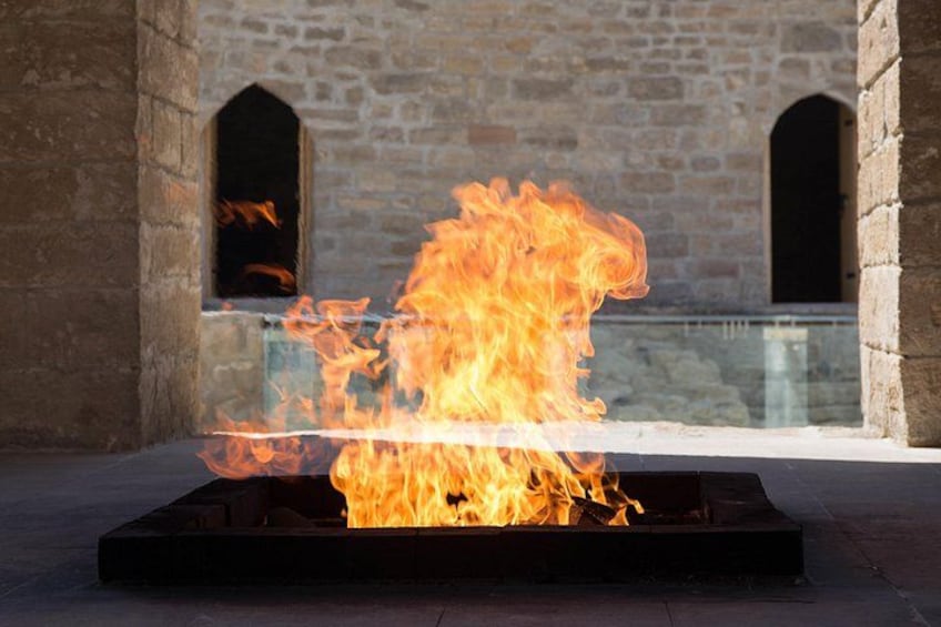 A fire burning in a metal container with stone walls and arched openings in the background. 2