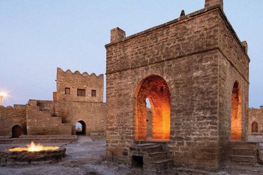 A stone structure with arched openings, a fire pit, and a distant castle. 1