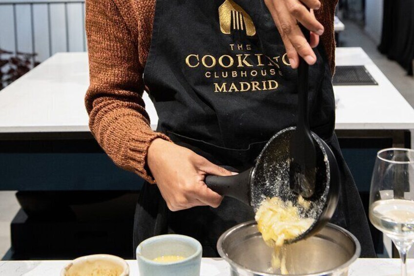 Una persona con delantal negro y el logotipo de 'The Cooking Clubhouse Madrid', preparando comida. 4