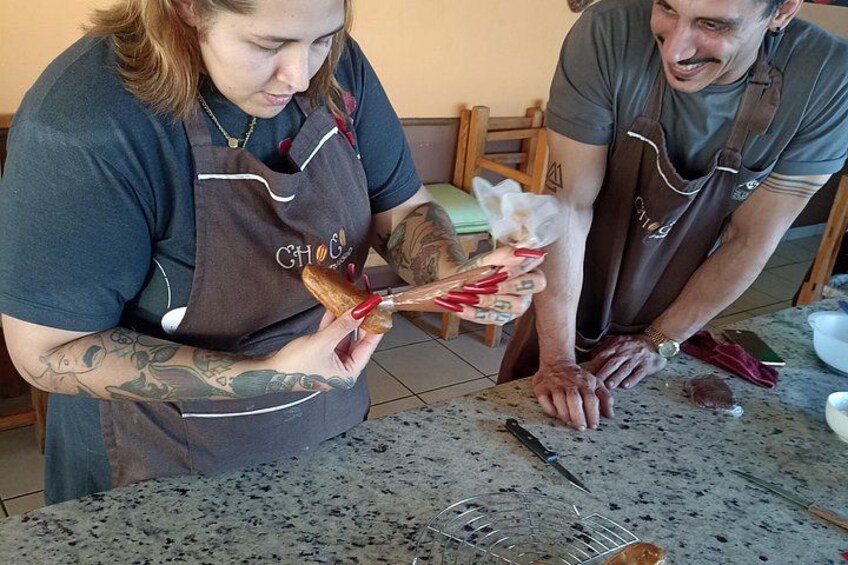 Two people wearing aprons, one holding a pastry and the other using a knife on a countertop. 5