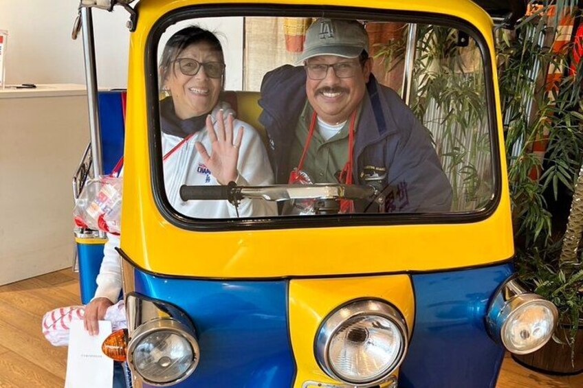 A yellow and blue tuk-tuk with two passengers inside. 4