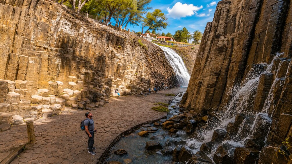 A waterfall in a rocky canyon with a paved walkway and a person standing on it. 5