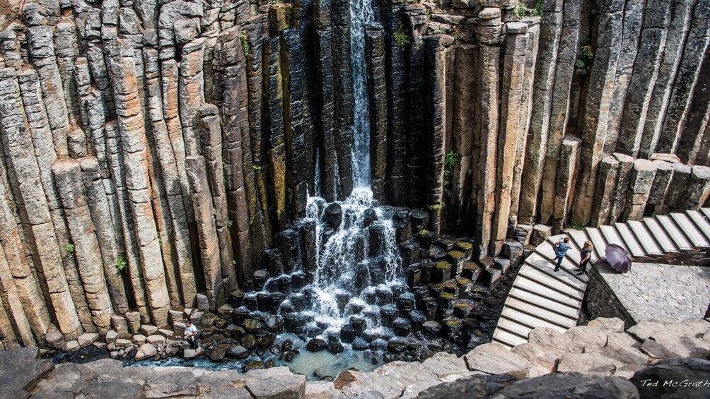 A waterfall cascading down a rocky cliff surrounded by stone steps. 1