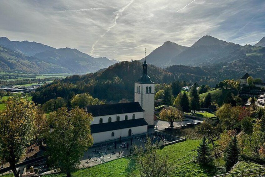 A church with a tall steeple, surrounded by green hills and trees. 4