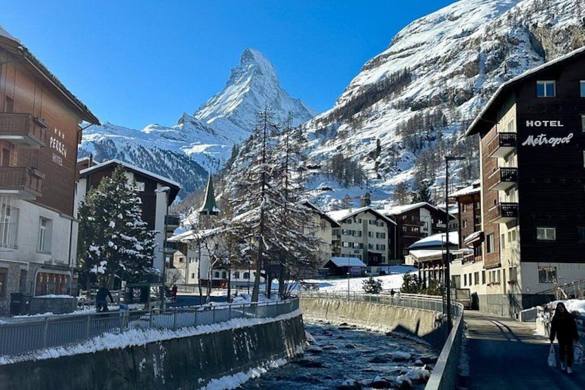 A snow-covered town with buildings, a river, and a mountain in the background. 1