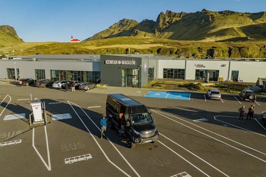 Un parking avec un autobus, un bâtiment portant l’inscription « Icewear Magasin », et un paysage montagneux en arrière-plan. 2