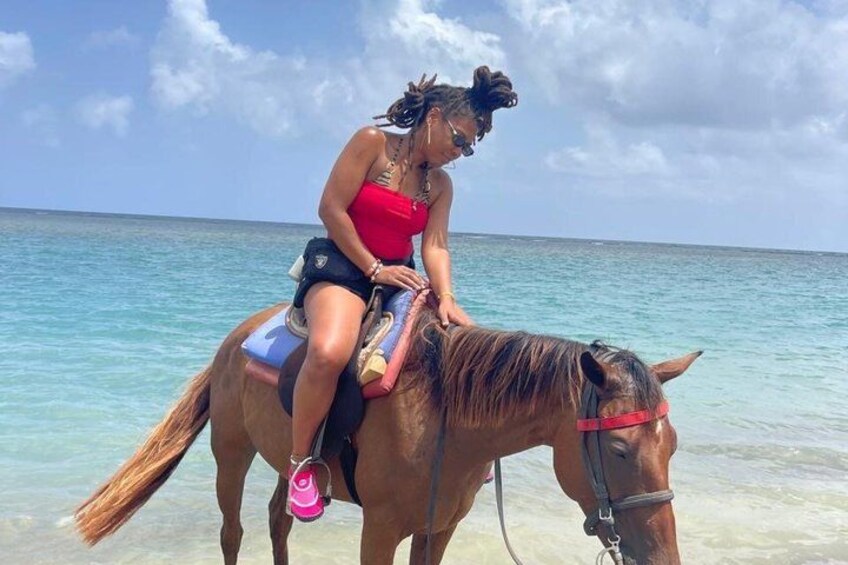 Eine Person reitet ein Pferd am Strand, im Hintergrund klares Wasser und ein wolkenloser Himmel. 4