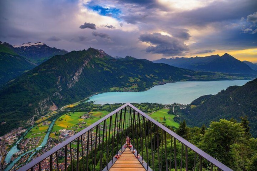 A wooden bridge with metal railings overlooking a mountainous landscape with a lake. 3