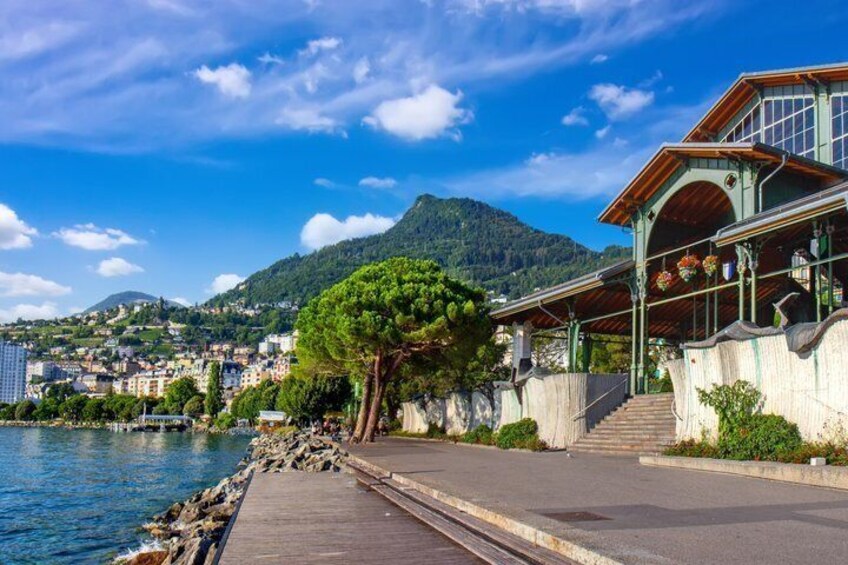 A waterfront promenade with a wooden walkway, a building with a green facade, and a mountain in the background. 1