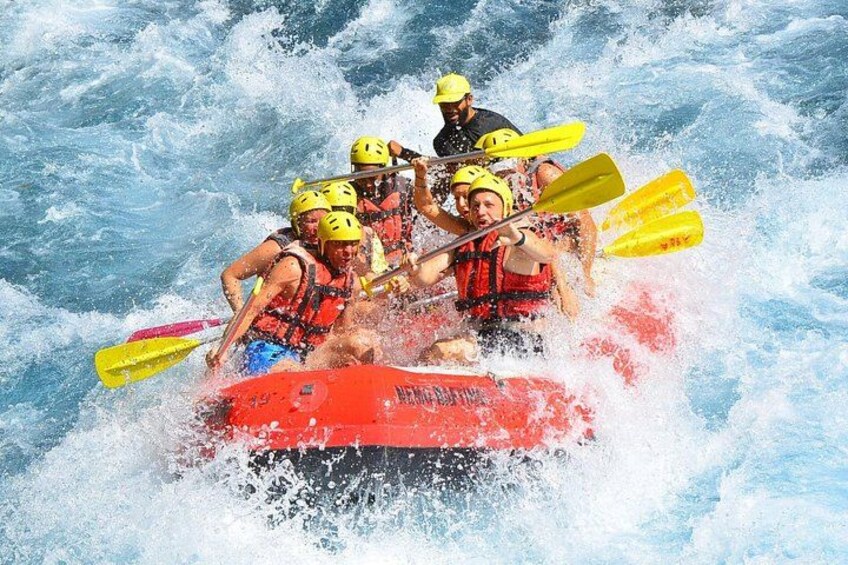 Een groep mensen in een rode raft die door woelig water vaart, met helmen en reddingsvesten. 2
